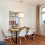 Essbereich mit Holztisch, weißen Stühlen und Fenster mit Vorhängen.