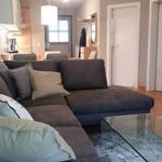 Ein Wohnzimmer mit grauem Sofa, Glas-Tisch und Küchenbereich im Hintergrund.