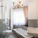 Badezimmer mit Badewanne, Dusche, Waschbecken und Fenster mit Vorhängen.