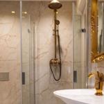 Bad mit Dusche, Marmorwand und goldfarbenem Waschbeckenhahn.