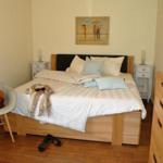 Schlafzimmer mit Bett, Nachttischen und Kleiderschrank. Wandbild und Sessel sind sichtbar.
