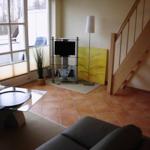 Wohnzimmer mit Glas-Tisch, Sofa, Fernseher und Holztreppe