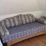 Ein Sofa mit Streifenkissen und Blumenmuster auf Holzrahmen in einem Raum mit Holzboden.