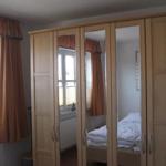 Schlafzimmer mit Spiegelschrank, Fenster und Vorhängen.