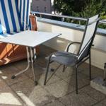 Terrasse mit blau-weißem Liegestuhl, Tisch und Stuhl. Geländer und Pflanzen im Hintergrund.