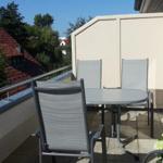 Terrasse mit Tisch und drei Stühlen, Blick auf Dächer und Bäume.