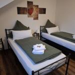 Zwei Betten mit grünen Decken und weißen Kissen. Wandbild mit Herz. Holzboden.