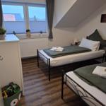 Zwei Betten mit grünen Decken, Fenster mit Jalousien und Holzboden.