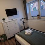 Zimmer mit Bett, Schrank, Fernseher und Fenster mit Blick auf Haus.