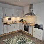 Moderne Küche mit weißen Schränken, Edelstahlherd und Mikrowelle.