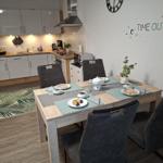 Esstisch mit Stühlen, Küchenbereich und Wanddekoration.