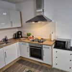 Küche mit weißen Schränken, Edelstahlherd und Mikrowelle.