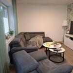 Wohnzimmer mit Sofa, Couchtisch und Fernseher. Grüne Vorhänge und Tapete.