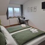 Schlafzimmer mit Doppelbett, Schreibtisch und TV. Fenster mit Jalousien und Wandbildern.