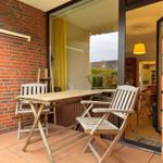 Terrasse mit Holztisch und Stühlen, rote Ziegelwand, Blick ins Haus.
