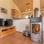 Wohnbereich mit Kaminofen, Fernseher und Küchenzeile im Hintergrund.