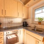 Küche mit Holzschränken, Edelstahlspüle und Fenster mit Pflanze.