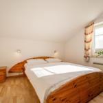 Schlafzimmer mit Holzbett, Nachttisch und Fenster mit Vorhängen.