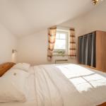 Ein Schlafzimmer mit Holzbett, Fenster mit Vorhängen und Kleiderschrank.