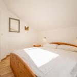 Schlafzimmer mit Holzbett, Spiegel und Nachttisch unter schrägem Dach.