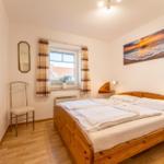 Ein Schlafzimmer mit Holzbett, Fenster, Vorhängen und Wandbildern.