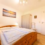 Schlafzimmer mit Doppelbett, Holzboden und Wandbild von Sonnenuntergang.