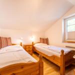 Zwei Einzelbetten mit Holzgestell, Nachttisch und Fenster mit Jalousie.