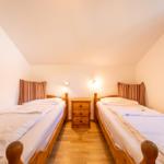 Zwei Einzelbetten mit Holzrahmen, Nachttisch und Wandlampen in einem Dachzimmer.