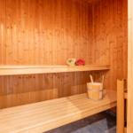 Sauna mit Holzwand, Bank und Eimer mit Löffeln.