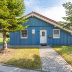 Blau gestrichenes Ferienhaus mit weißen Fenstern und Tür. Vor dem Haus liegt ein gepflasterter Weg.