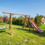 Holzspielplatz mit Rutsche, Schaukel und Klettergerüst auf grünem Rasen.