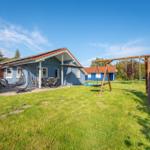Blau gestrichenes Ferienhaus mit Spielplatz und Terrasse im Garten.