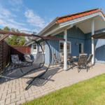 Terrasse mit Sitzgelegenheiten und Sonnenschutz vor einem blauen Haus.