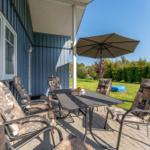 Terrasse mit Tisch, Stühlen und Sonnenschutz unter blauem Himmel.