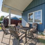 Terrasse mit Tisch und Stühlen, blauer Hauswand und Garten im Hintergrund.