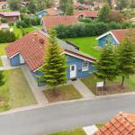 Blau gestrichenes Haus mit rotem Dach und grünem Garten. Neben ihm ein weiteres Haus.