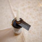 Eine Kerze in einem Glasbehälter mit Etikett und Schnur auf Tischdecke.