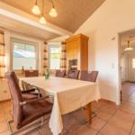 Esszimmer mit Holzdecke, Tisch mit Tischdecke und Stühlen, Fenster mit Vorhängen.