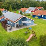 Blauer Ferienhaus mit Solaranlage, Terrasse und Spielplatz auf grünem Grund.