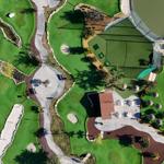 Aerial view of a golf course with green areas, sand traps, and a building.