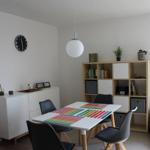 Esszimmer mit Tisch, Stühlen und Regal. Deckenleuchte und Wanduhr sind sichtbar.