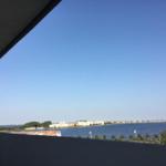 Blick vom Balkon auf einen See mit Uferbebauung und klarem Himmel.