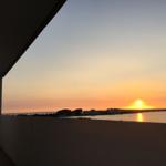 Sonnenuntergang über dem Wasser mit Blick auf Gebäude und Bäume von der Terrasse aus.