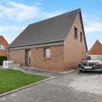 Modernes Haus mit Steinmauer, Garage und gepflasterter Auffahrt. Grünflächen und klare Sicht.