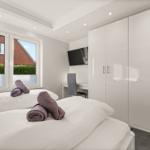 Zimmer mit Doppelbett, Schrank und Fenster mit Blick auf Garten.