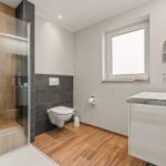 Badezimmer mit Dusche, Toilette und Waschbecken. Holzboden und Fenster.