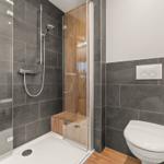 Dusche mit Glaswand, Toilette und Holzbank in moderner Badezimmerausstattung.