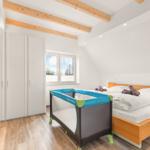 Schlafzimmer mit Doppelbett, Kinderbett und Kleiderschrank unter Dachschrägen.