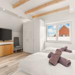 Schlafzimmer mit Doppelbett, TV, Kleiderschrank und Fensterblick auf Haus.