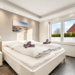 Schlafzimmer mit weißem Bett, Nachttisch und Fenster mit Blick auf Garten.